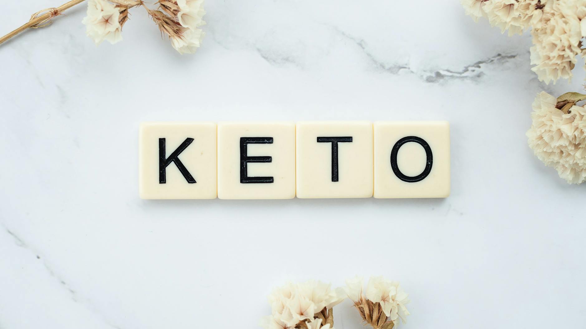 Przygotowanie do wlewu witaminowego a dieta ketogeniczna, wege i low carb Kafelki Scrabble układające się w napis Keto na marmurowym tle z kwiatami
