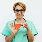 Czy dożylne podanie magnezu i potasu może być niebezpieczne dla osób z arytmią Lekarka w scrubach trzyma papierowe serce, uśmiecha się z stetoskopem