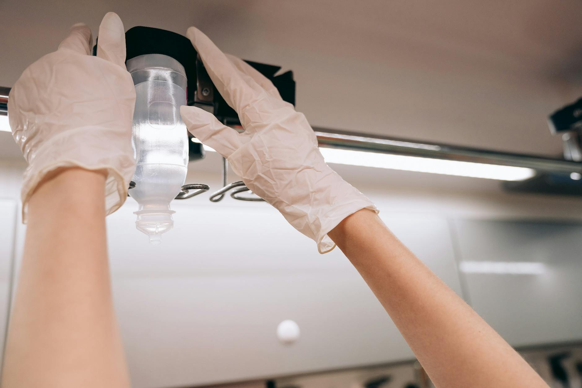Ręce w rękawiczkach regulujące kroplówkę witaminową w gabinecie
