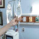 Jak łączyć mikroelementy i aminokwasy w jednej kroplówce, by uniknąć niekorzystnych interakcji Dłoń pacjenta z podłączoną kroplówką w szpitalnym pokoju