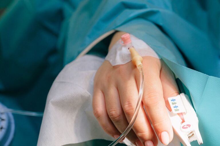 Dłoń pacjenta z kroplówką dożylną i pulsoksymetrem